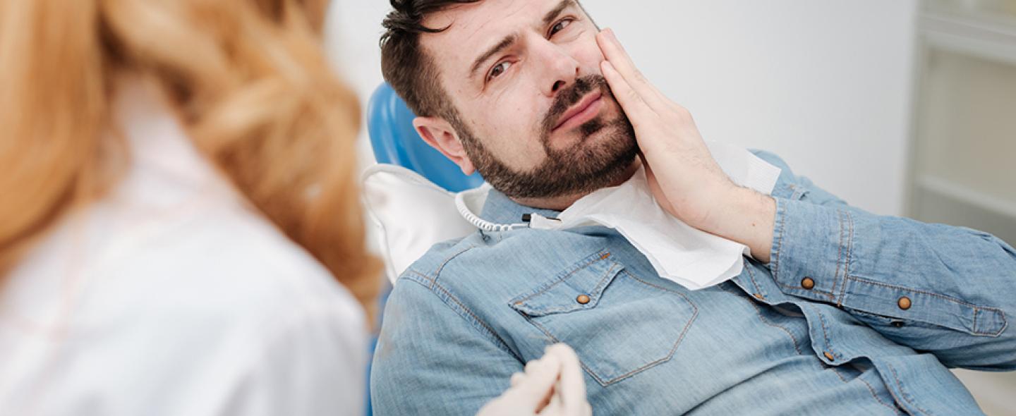 Hammassärystä kärsivä miespotilas pitelee poskeaan hammaslääkärin vastaanotolla