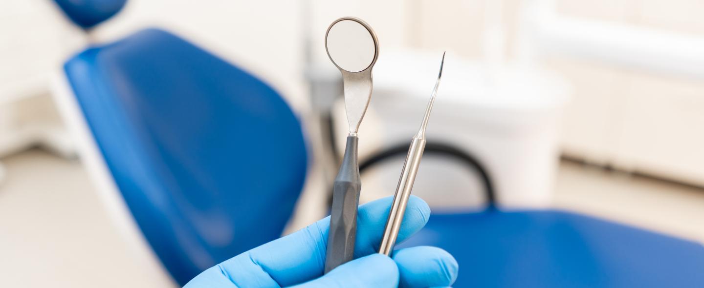 Instrumentteja hammaslääkärin kädessä ja taustalla tyhjä potilastuoli